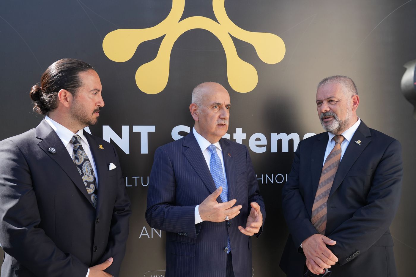 ANT Systems logosunun önünde konuşan üç kişi.
