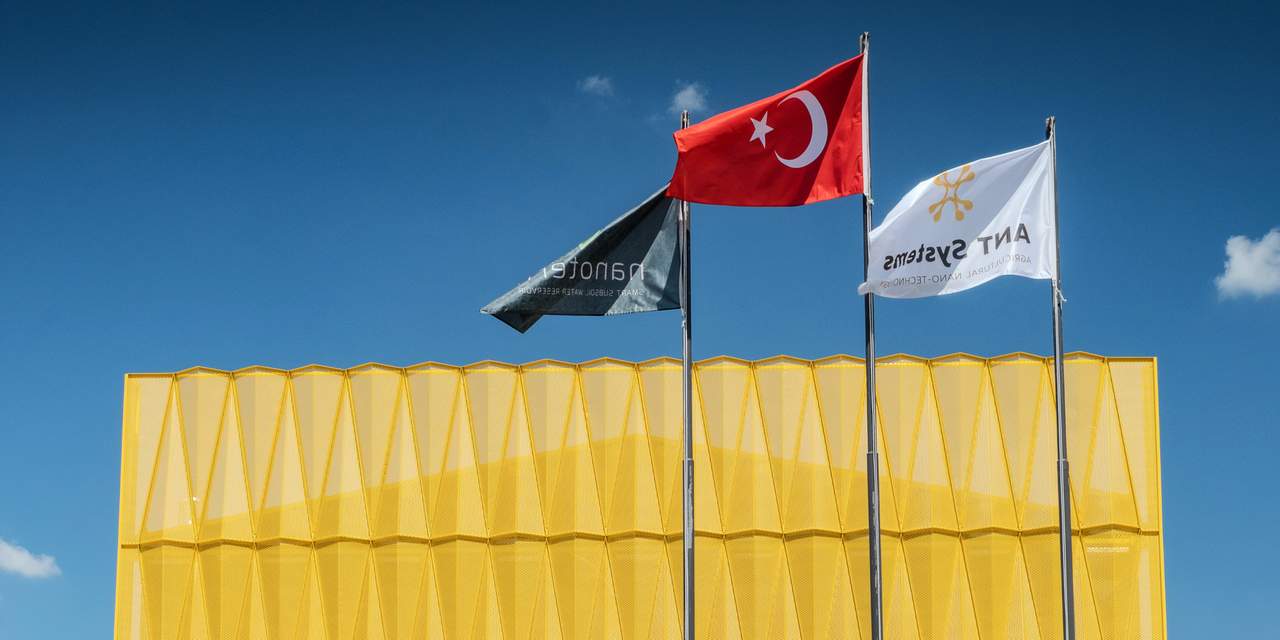 ANT Systems fabrikasının sarı cephesi ve bayrakları.